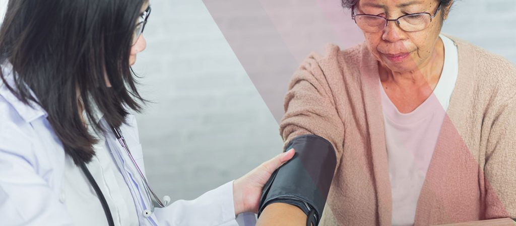 A doctor in a white coat checks an older woman's blood pressure with an upper-arm cuff during a health screening.